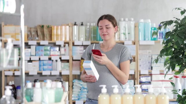 Adult pregnant woman scans mobile barcode of moisturizing lotion on the background of shelves in pharmacy . High quality 4k footage