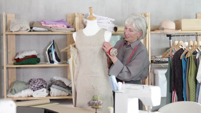 Attentive mature female dressmaker working with tailor's dummy in sewing workshop 