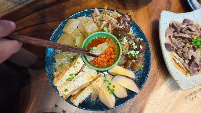 Dipping Braised Pork Belly and Tofu into Chili Sauce with Chopsticks