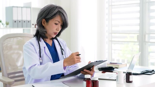 Stressed Female doctor nurse sit by laptop computer while reviewing patient medical charts at the clinic office.