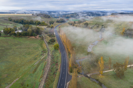 Winding country road cutting through a mist‑covered rural landscape