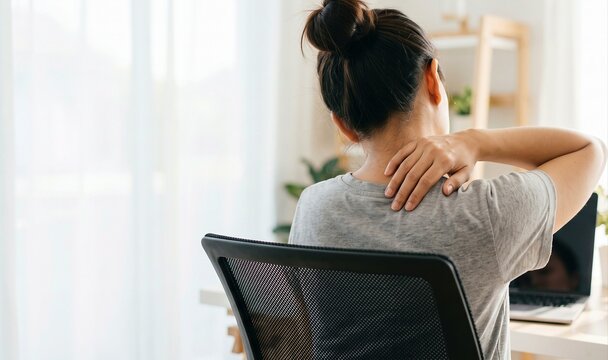 Woman massaging painful neck and shoulder at home office desk, poor posture health issue.