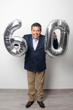 60-year-old Latino man with a dark skin displays 60 shaped balloons to celebrate his birthday and his entry into his old age