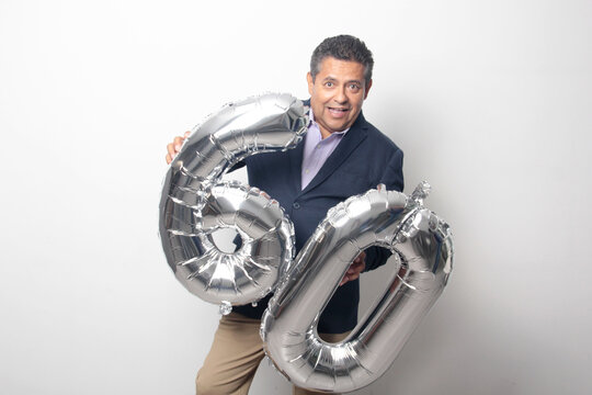 60-year-old Latino man with a dark skin displays 60 shaped balloons to celebrate his birthday and his entry into his old age