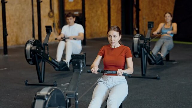 Woman exercises on a rowing machine in the gym. European is preparing for the rowing competition. Fitness club client at a group cardio workout 