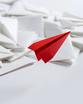 Rotes Papierflugzeug hebt sich aus wei&szlig;en Formen als Symbol f&uuml;r Mut und neue Wege