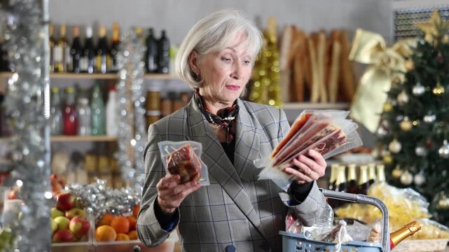 Elderly woman buyer chooses packaged jamon in christmas decorated grocery store 
