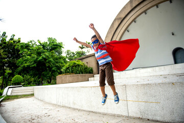 Young boy in superhero costume jumping outdoors with red cape © Rawpixel.com