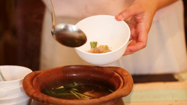 Serving Traditional Thai Isan Soup from Clay Pot into Bowl