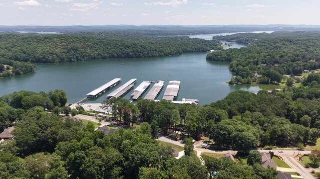 Aerial view of a lakeside marina in Soddy Daisy Tennessee. Long rows of covered boat slips reach out over blue green water while forested hills and a hazy summer sky surround the harbor.