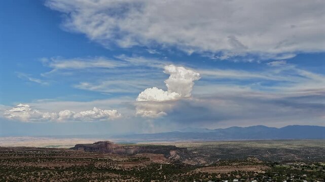 4K drone timelapse of a dramatic pyrocumulus wildfire plume building in the distance. The isolated white smoke column rises above a vast southwestern high desert canyon and mesa landscape.