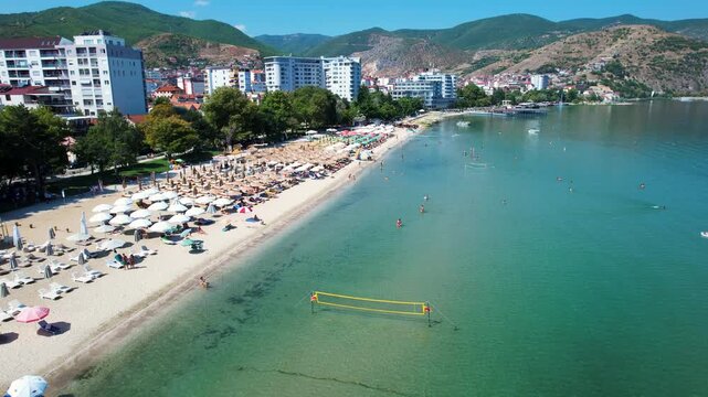 People vacation swimming and sunbathe under colorful umbrellas on Pogradec city beach Ohrid lake