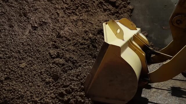 Hydraulic loader bucket digging into raw clay pile inside old Japanese tile factory