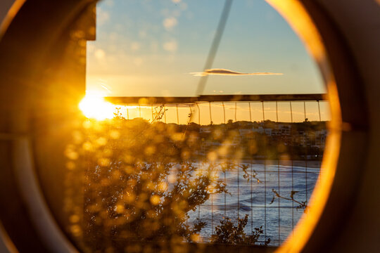 Golden sunset over ocean and coastal neighbourhood creatively framed through circular opening
