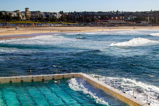 Ocean waves crashing beside outdoor swimming pool overlooking sandy beach and coastal neighbourhood