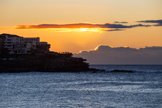 Golden sunset behind layered clouds over the ocean with silhouetted people watching