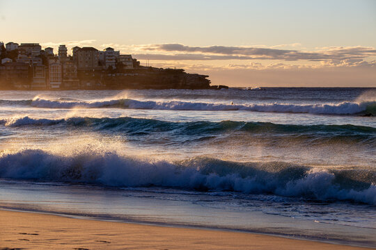 Powerful ocean waves breaking along sandy beach with coastal buildings and rocky headland
