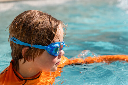 Young boy swimming in the pool wearing light blue goggles and an orange rash guard