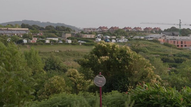 Sopelana coastal village on a hillside with residential homes, lush green vegetation, and a visible construction crane