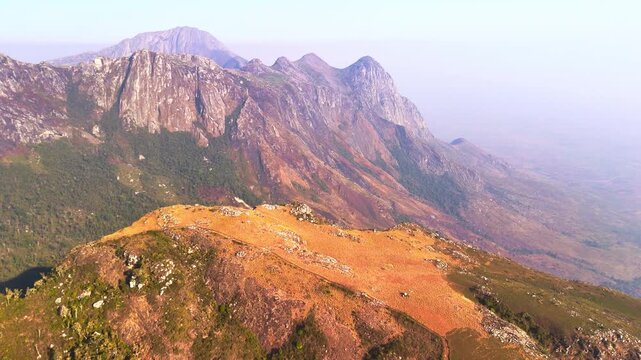 Drone flies toward a rugged mountain edge, revealing a towering peak and deep green valley within the remote wilderness of Mulanje, Malawi.