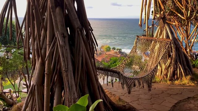 Empty rope hammock hanging between pandan trees with a view of the ocean coastline