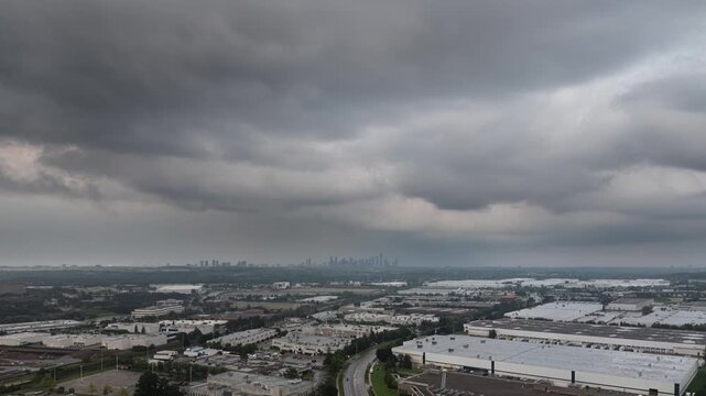 Dark storm clouds roll rapidly over warehouse buildings in Ontario. The distant city skyline is silhouetted against the dim, threatening sky during a summer storm.
