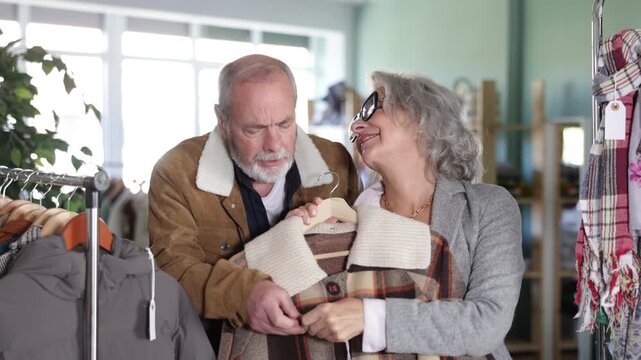 Mature couple spend time in shop and choose down jacket or checkered coat. Changing wardrobe, shaping style of clothing. Designer clothes, clothing of world brands 
