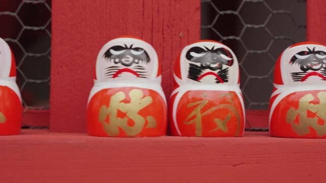 Close-up footage reveals rows of small Daruma dolls carefully arranged inside weathered wooden compartments, highlighting their distinctive faces, colors, and traditional symbolism.