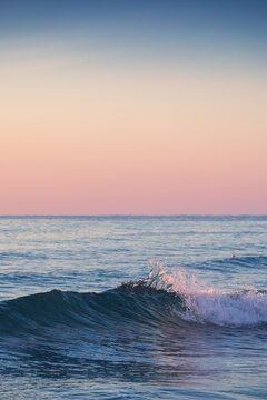 Vertical view of ocean wave crest splashing under pastel pink and blue twilight sky