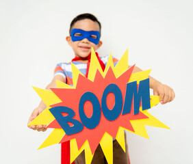 Child in superhero costume holding a 'BOOM' sign, smiling. © Rawpixel.com