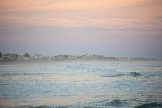 Misty Coastal Town and Ocean Waves at Pastel Sunset