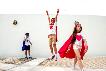 Kids in superhero costumes jumping and posing energetically outdoors. © Rawpixel.com