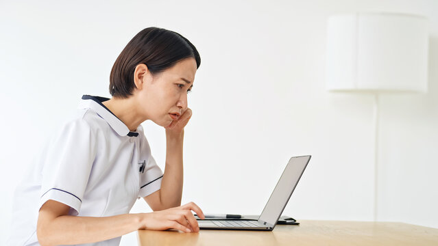 ノートPCを見て悩む白衣の女性。看護師、介護士、医療事務、不満、不安、心配、疑問、DX、落ち込む