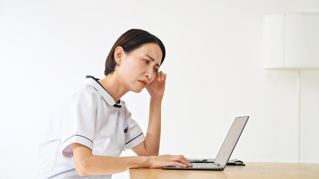 ノートPCを見て悩む白衣の女性。看護師、介護士、医療事務、不満、不安、心配、疑問、DX、落ち込む