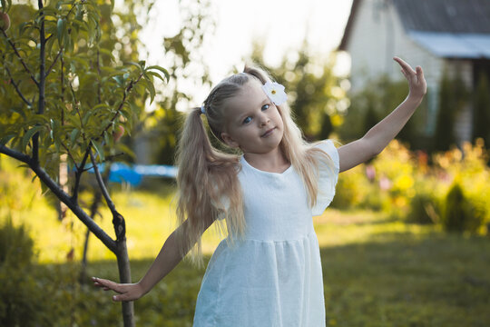 a cute five-year-old girl in a white dress is playing in a green summer garden. happy childhood