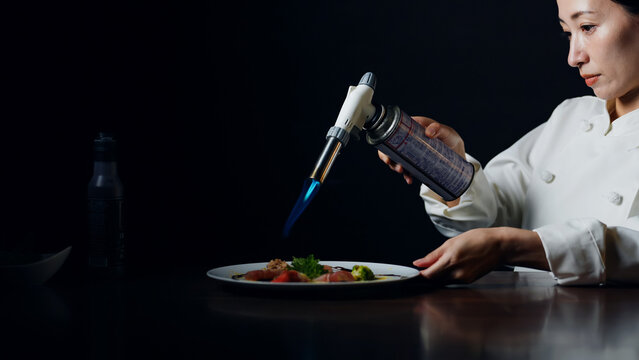 バーナーで料理を炙る女性シェフ。レストラン、調理師、フレンチ、イタリアン、コース、高級、美食、飲食店