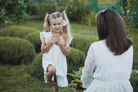 a cute five-year-old girl with mother in a white dress are playing in a green summer garden. happy childhood