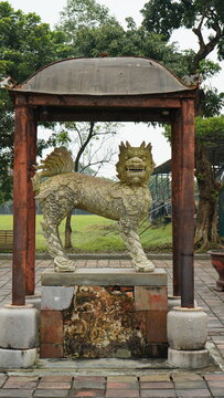Weathered Stone Qilin Guardian Statue Framed by Rustic Iron Gate at Hue Royal Tomb, Vietnam