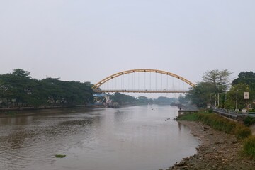 Fototapeta premium Pekanbaru, Riau, Indonesia—August 25th, 2026: View of Siak III Bridge over the low-water Siak River enveloped in wildfire smoke and haze during the dry season, with the silhouette of Siak IV Bridge