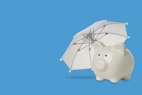 Insurance. Piggy bank rests beneath white umbrella, symbolizing protection and savings