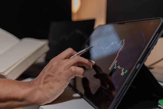 Professional trader analyzing stock market charts across multiple screens using laptop and tablet to monitor price movements, technical indicators and investment strategies in modern trading workspace