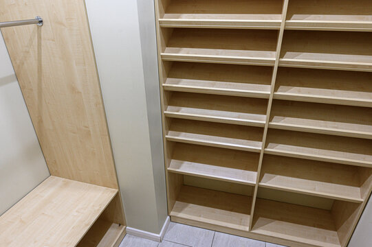 Light‑oak built‑in wardrobe with dual‑column open shelves, a bench seat, and a hanging rail. clean joinery and minimalist design maximize storage in a compact layout