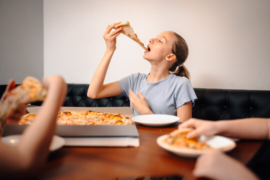 Young girl eating pizza slice with friends