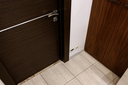 Dark walnut‑finish interior door with sleek silver handle and linear accent. paired with matching cabinetry, light tile flooring, minimalist wall socket detail