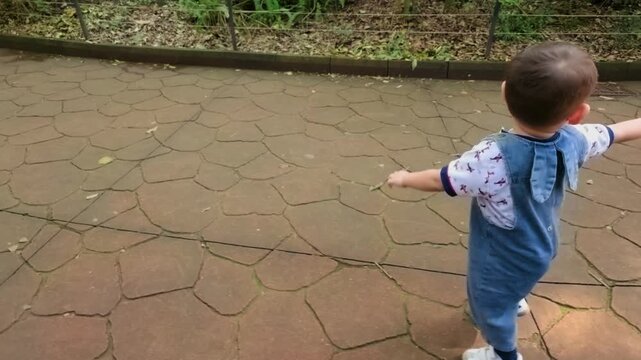 A young Latina mother and her 2-year-old baby enjoy a day at the zoo. The baby excitedly rushes ahead, eager to see their favorite animal, while the mom catches up pushing a stroller.