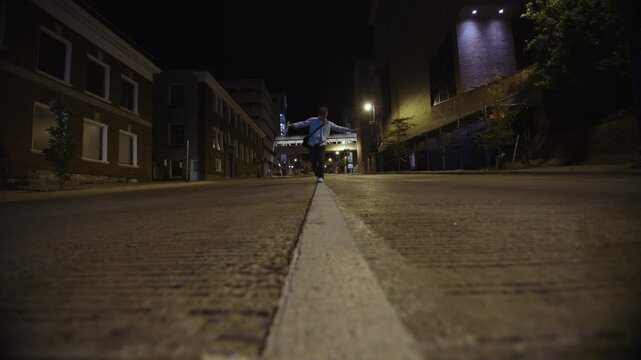 Young man with a bottle of alcohol walking on a street line trying to keep his balance at night