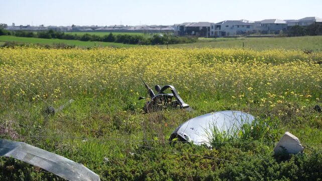 Discarded car debris and illegal rubbish dumping in a field of undeveloped rural land, with modern suburban housing developments in the background in Truganina, Melbourne, Australia.