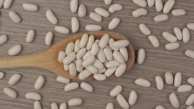 A captivating close up view of dry cannellini beans on a rustic wooden table with a wooden spoon showcasing organic legumes in dynamic motion.