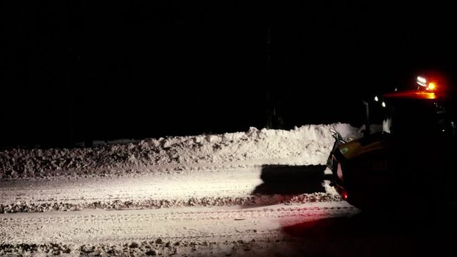 Heavy machinery with flashing lights plowing a rural road during a winter blizzard at night. Municipal services vehicle ensuring transportation safety and accessibility after a heavy snowfall