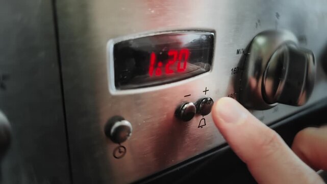 Male finger presses timer button on gas stove panel to set alarm, minutes. Man setting cooking timer appliance control panel kitchen, domestic gas oven stove. Household task meal preparation